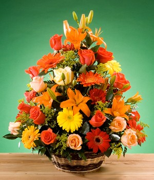arreglo de rosas gerberas y otras flores en tonos amarillo y naranja en canasta